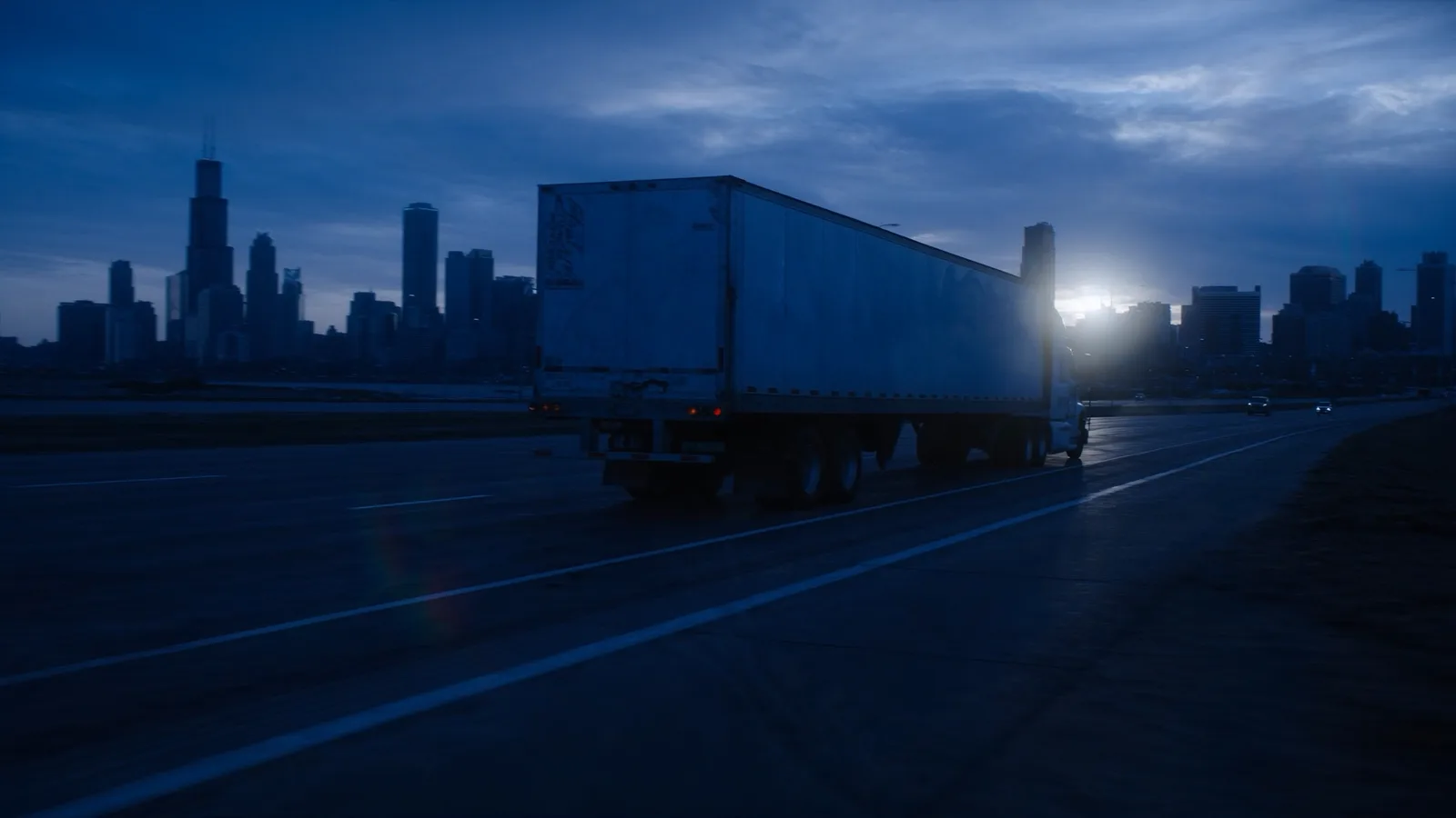 A 53ft dry van running an interstate at blue hour with the Chicago skyline behind it